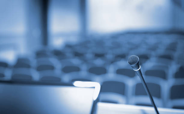 istock Rostrum with microphone and computer in conference hall, blue toned 1344997627