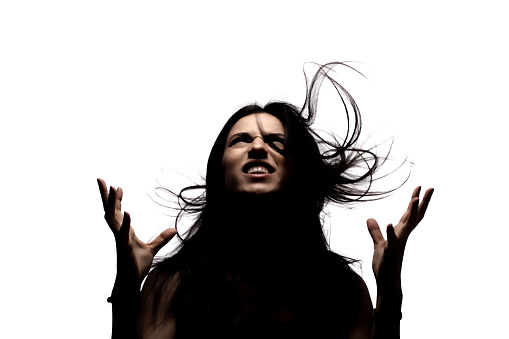 Dark portrait with shadows of an angry girl with hair in the air looking up and making gestures with her hands.