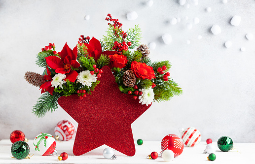 Festive winter flower arrangement in vase of red star shape and Christmas decorations on table.