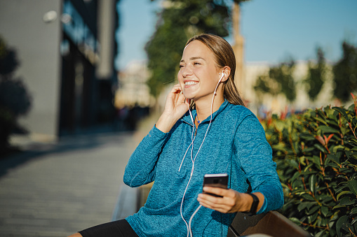Young smiling woman holding a mobile phone in her hand and listening to music