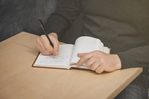istock The man's hand holds a pen and writes in a notebook. The second hand is holding the notebook. 1345006863