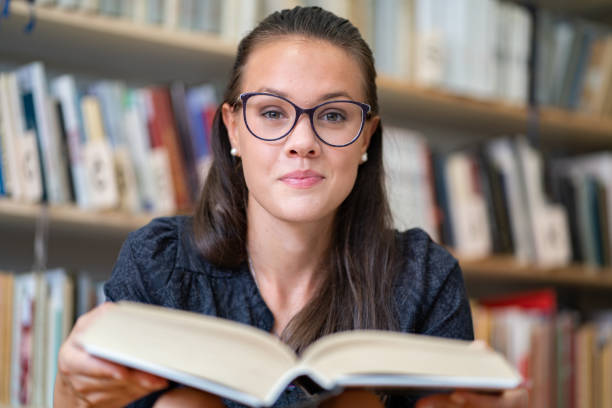 bella giovane donna ritratto che tiene un libro aperto in una libreria - student effort book carrying foto e immagini stock