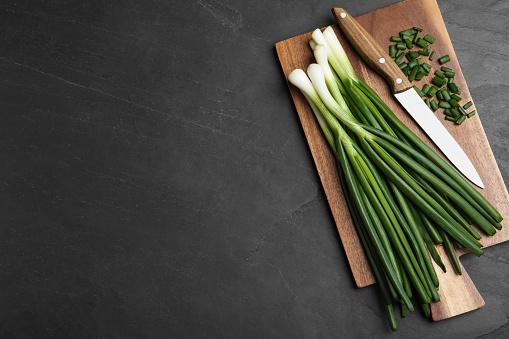 Fresh green spring onions, cutting board and knife on black table, top view. Space for text