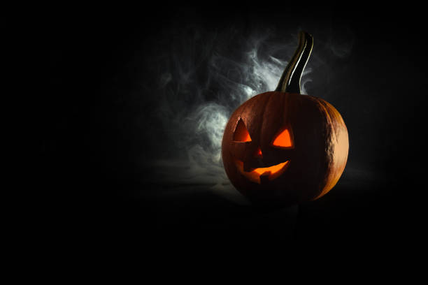 istock Halloween, orange pumpkin with luminous face on a blackbackground. Thick smoke comes out. 1345009830