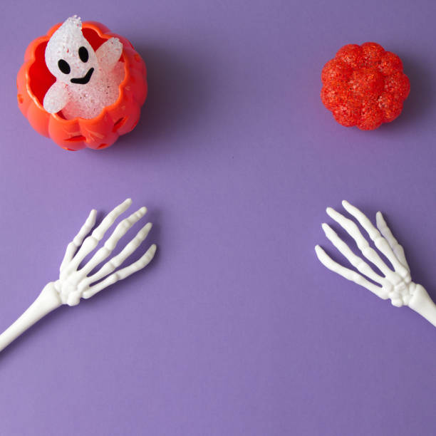 istock Pumpkins for Halloween with a ghost on a purple background with hand bones with copy space. Minimal aesthetic flat lay. 1345011309