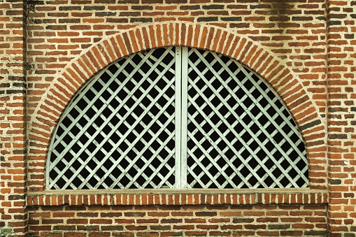 An old white arched window, made of wood, diagonally and an exposed brick wall.