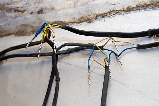 Connection of wires against the background of a wall in a house under construction. Twisting, soldering, welding of electrical cables.