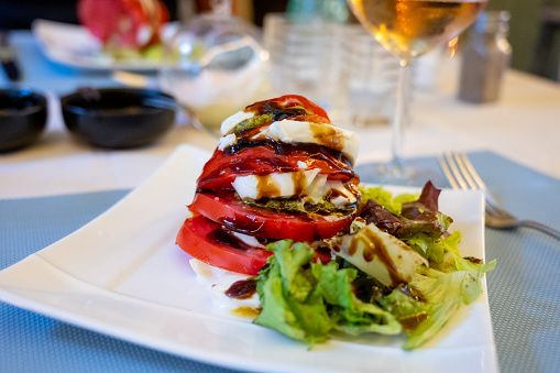 Big red french tomato served with fresh mozzarella cheese, basil pesto and creme balsamico as starter in small restaurant in Provence, France