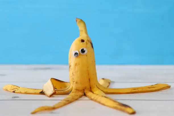 Photo of Close-up image of funny, cartoon monster octopus made from ripe, banana with googly eyes and strips of peel used to make tentacles, blue background, children healthy eating, humorous concept