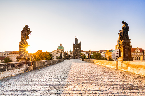 Panoramic view of castle, cathedral of Prague and historical buildings in old town of Prague, taken from one of the sides of Charles Bridge. There is a black street light standing at the bridge in the front and at the left side the famous John of Nepomuk Statue is standing.