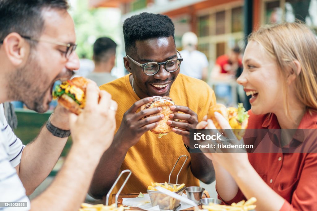 Friends and fast food Friends eating burgers and fries and have fun in outdoor restaurant Eating Stock Photo