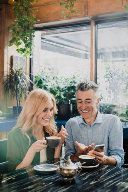 istock Vertical portrait of two heterosexual spouses romantic couple colleagues watching using smartphone on a date in cafe restaurant while drinking coffee in the morning. 1345015106