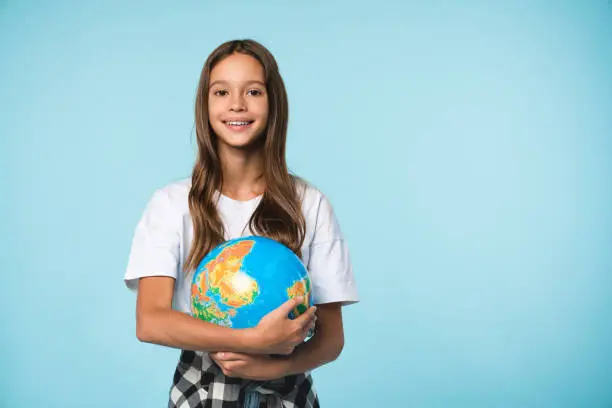 Caucasian young teenager schoolgirl pupil student holding hugging globe on geography lesson isolated in blue background. Happy Earth day!