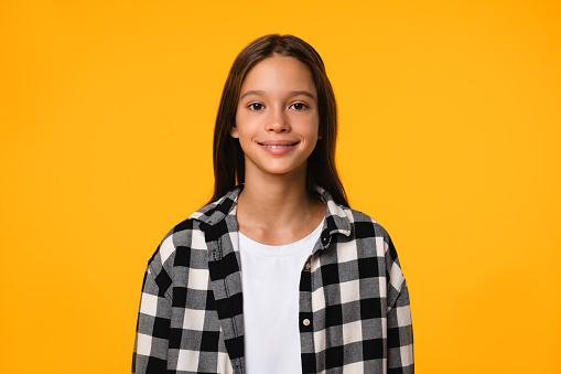Cheerful smiling young lady teenager girl schoolgirl in plaid shirt looking at camera in the yellow background. Caucasian teenage girl cutout portrait.