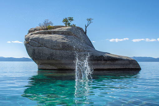 An image of Bonsai Rock in Lake Tahoe, Nevada. The image looks west as a rock splases infront of Bonsai Rock on a amazing day in October.