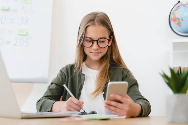 istock Little schoolgirl pupil student e-learning, using smart phone for remote education, checking homework, preparing for test lessons indoors from home on lockdown 1345027789