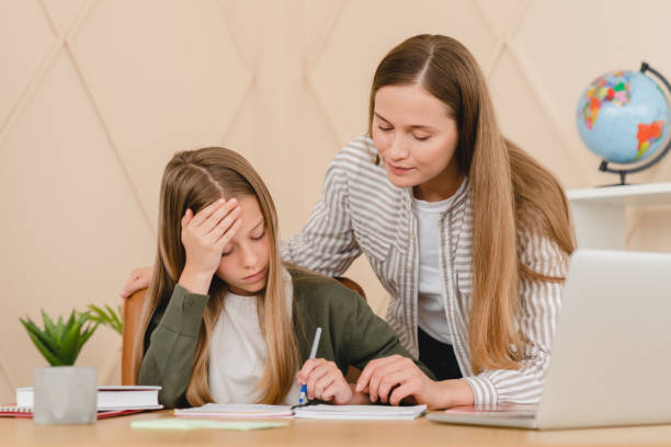 Hard stressed sad overworked student schoolgirl pupil doing difficult task homework while tutor teacher mother helping with school preparation. Hard stressed sad overworked student schoolgirl pupil doing difficult task homework while tutor teacher mother helping with school preparation. Online Childcare Training stock pictures, royalty-free photos & images