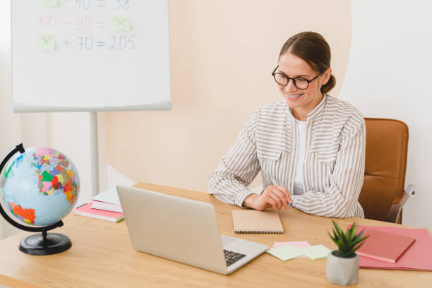 istock Young teacher tutor student on online remote lesson using laptop, listening to the schoolchildren students, writing checking homework at school classroom. 1345027935