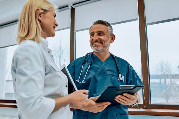 istock Two beautiful doctors are holding a folder and tablet, looking at each other and smiling, standing in the hall of the hospital. 1345030905