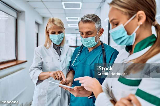 Three Doctors In Protective Mask With A Tablet On The Corridor Of The Hospital Checking Something Stock Photo - Download Image Now
