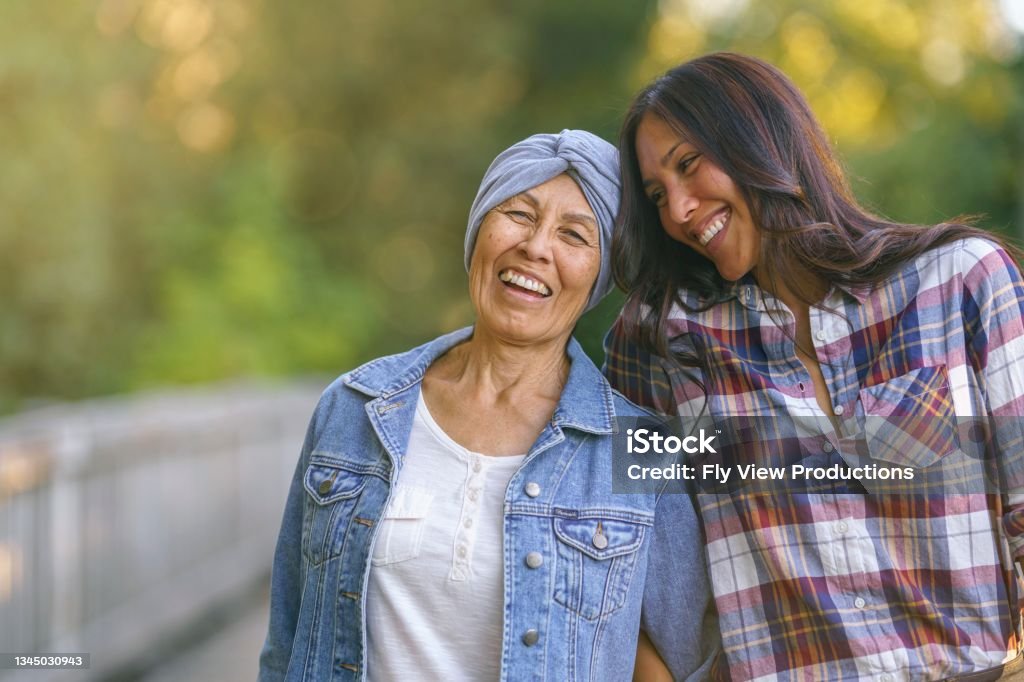 Happy senior woman with cancer laughing with daughter An woman embraces her senior mother with cancer. They are outside and both are smiling and happy to be together. The daughter is looking toward her mom affectionately. Cancer - Illness Stock Photo