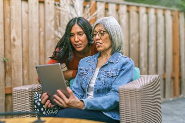 donna anziana che impara a usare il tablet con l'aiuto di sua figlia adulta - senior adult computer senior women women foto e immagini stock