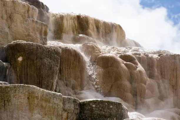 Water flowing off mineral deposit mounds with clouds and blue sky in the background.