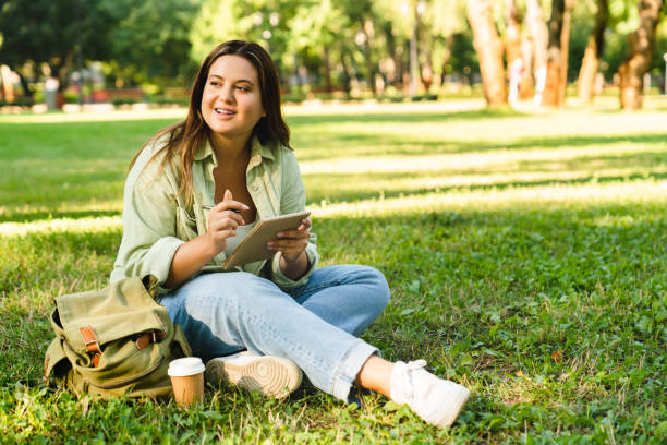 istock Caucasian young freelancer woman student doing homework, e-learning, preparing for test exam, writing poems novels relaxing on college university lawn park 1345038821