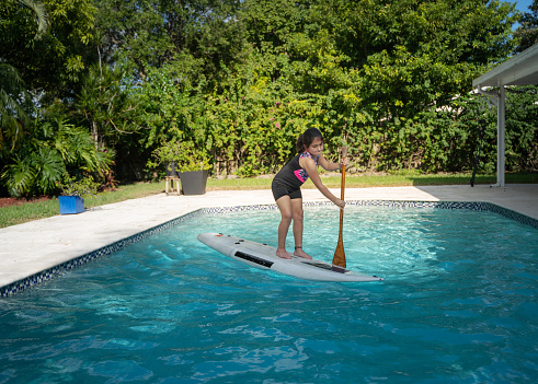 Cuban american girl learning to stand up in paddle board on a swimming pool