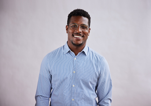Portrait of a young African American businessman wearing glasses and smiling while standing against a gray background