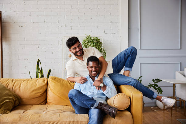 giovane coppia gay che ride rilassandosi insieme a casa - gay man homosexual couple homosexual men foto e immagini stock