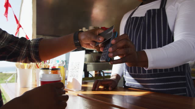 Midsection of african american man paying male owner for coffee by credit card at food truck