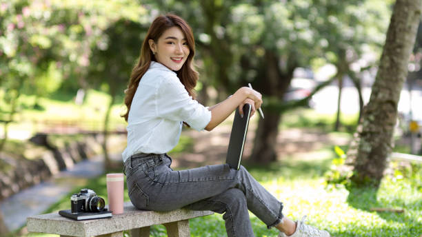 istock Beautiful female sat on a stone bench with a digital tablet in a greenery park. 1345052226