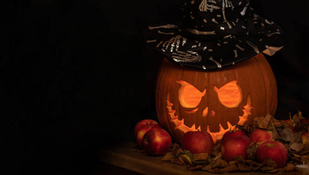 istock carved orange pumpkin on dark background. Jack-o-lantern with black hat setting mood for trick-or-treaters. 1345056373