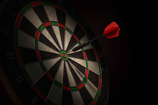 Darts 3D illustration of a shiny black dart with a red flight hitting the bulls-eye of a dartboard. dartboard stock pictures, royalty-free photos & images
