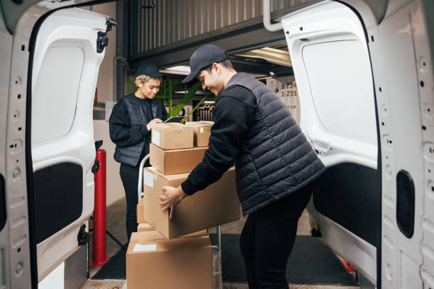 istock Side view male courier loads cardboard boxes from cart into the car while coworker checking information on digital tablet 1345064516