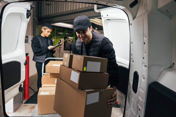 istock Smiling male courier loads cardboard boxes from a cart into the car while coworker checking information on digital tablet in warehouse 1345064556