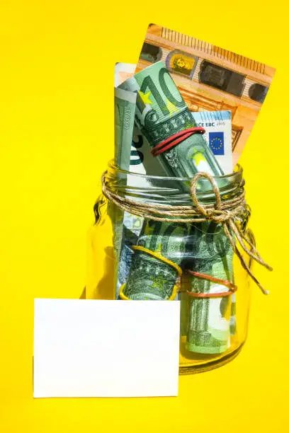 Photo of Glass jars filled with Euro bills, savings inside glass jar, money isolated on yellow background, copy space for text. Paper note. Business budget of wealth