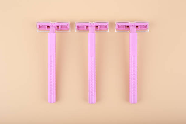 Top view of three pink razors in a row on light beige background. Concept of smooth skin, shaving and epilation