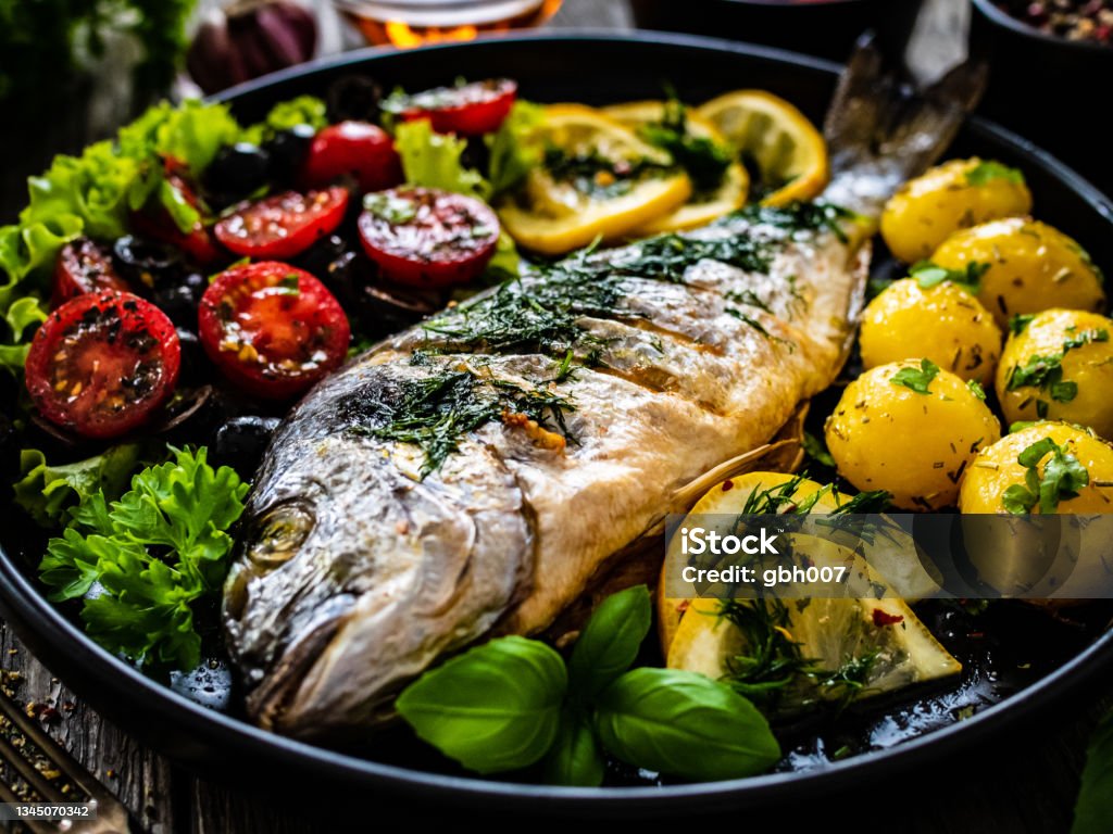 Fish dish - roasted sea bream with vegetables on wooden table Fish dish - roasted dorada with vegetables on wooden table Trout Stock Photo