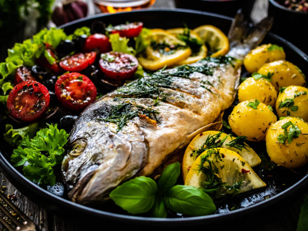 Fish dish - roasted sea bream with vegetables on wooden table Fish dish - roasted dorada with vegetables on wooden table trout stock pictures, royalty-free photos & images