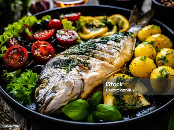 Fish Dish Roasted Sea Bream With Vegetables On Wooden Table Stock Photo - Download Image Now