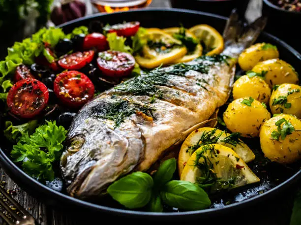 Fish dish - roasted dorada with vegetables on wooden table