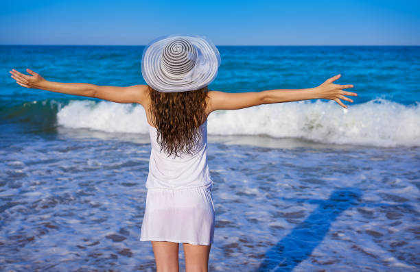 istock Girl with beach hat in sea open arms 1345070364
