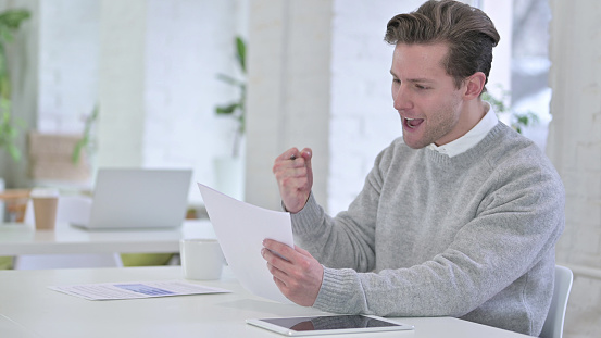 Creative Young Man Celebrating Success on Documents
