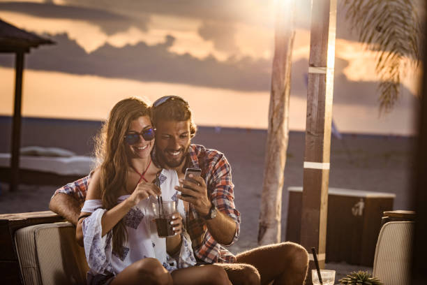 istock Happy couple using mobile phone in a beach bar at sunset. 1345071907