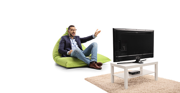 Man sitting on a green bean bag chair, gesturing with hand and watcing tv isolated on white background