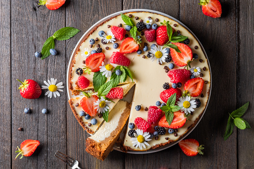 Cheesecake pie with fresh berries, strawberries, blueberries and blackberries and mint chamomiles in a round plate