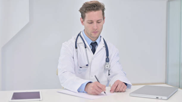 istock Writing Young Doctor Doing Paperwork in Clinic 1345073047