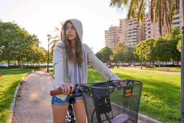 Brunette girl riding bike in the park with hoodie sweater